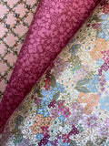 Three rolls of patterned fabric stacked diagonally. The top-left roll is light pink with a dark green trellis pattern.