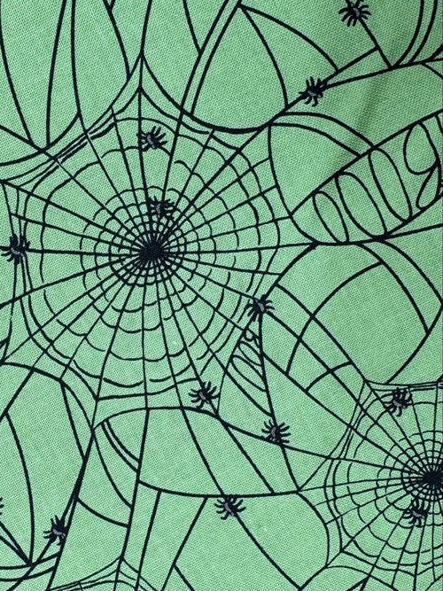 Green fabric with black spider web pattern on a wooden surface