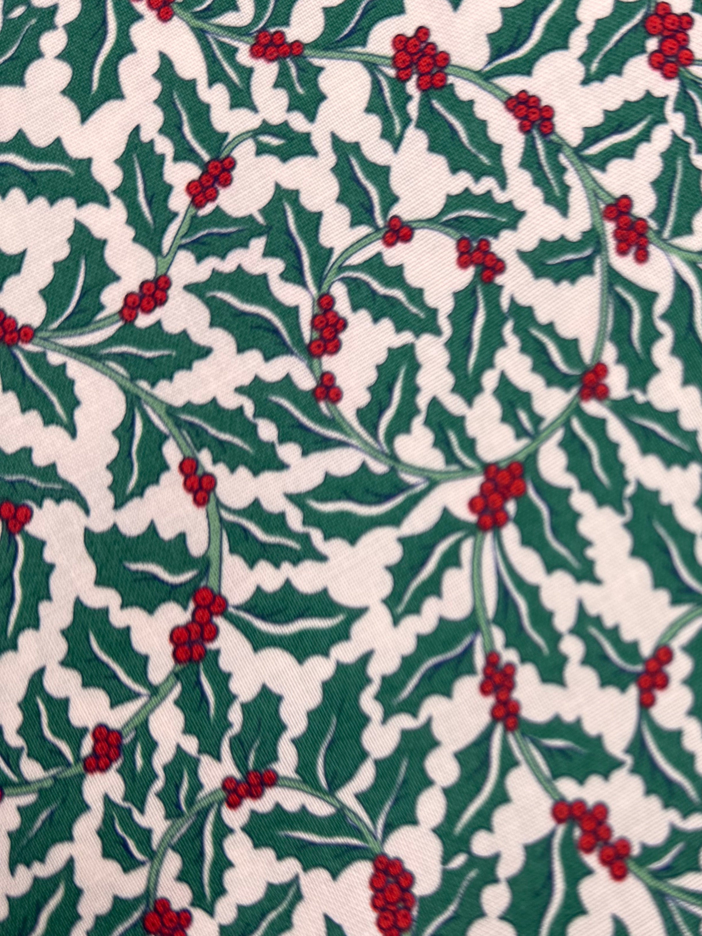 Christmas-themed fabric with holly leaves and berries on a wooden surface