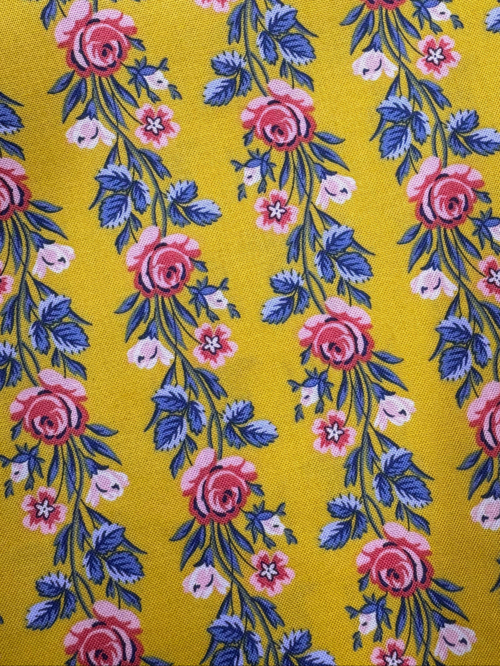Floral fabric with pink and blue flowers on a yellow background, placed on a wooden surface.
