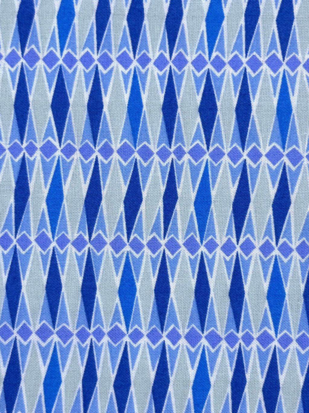 A close-up of a woven fabric with a repeating geometric pattern of blue and purple diamonds on a light gray background.
