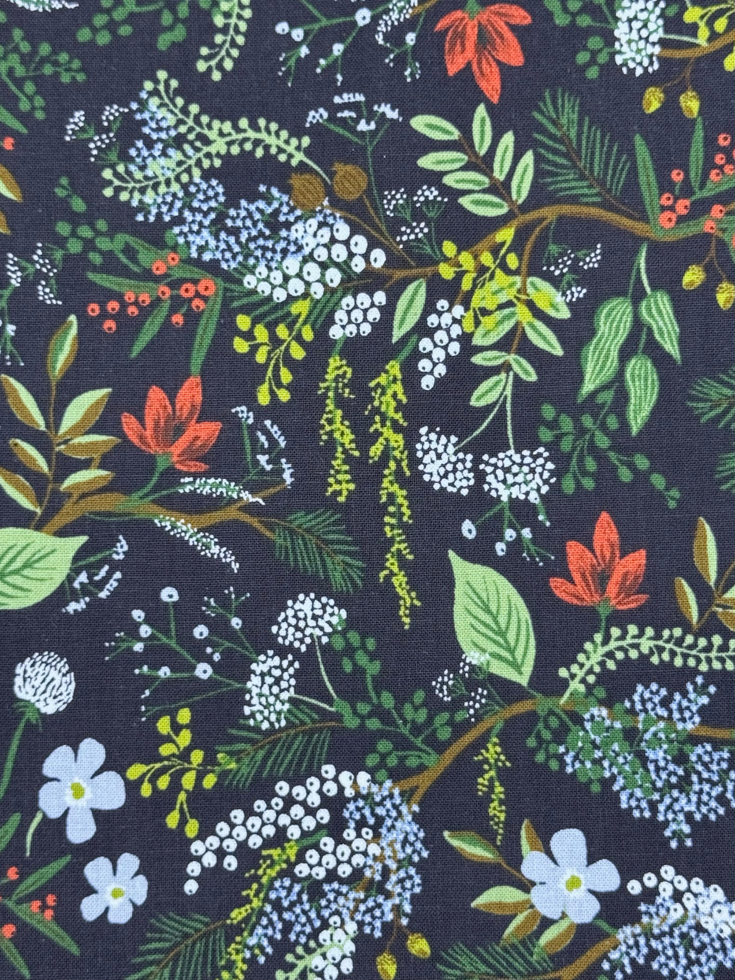 A close-up of a dark black fabric with an all-over botanical print featuring green leaves, white and light blue flowers, and small red accents.
