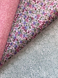 Three folded fabric samples displayed diagonally, showing different patterns: a pink damask pattern, a light pink floral print with purple and blue flowers, and a sage green fabric with white polka dots.