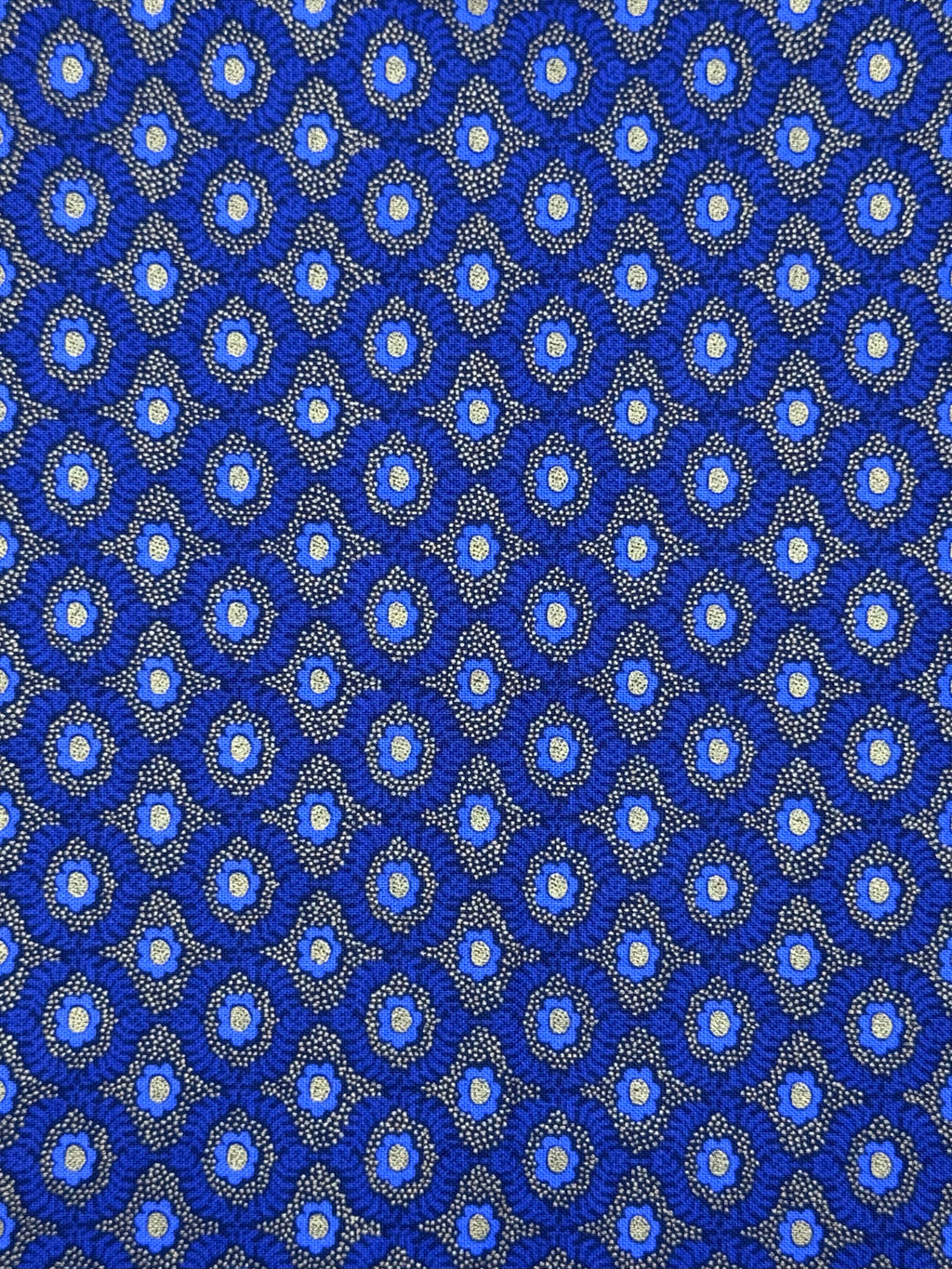 A close-up of a repeating blue patterned fabric or material with small circular motifs and fine dotted details in white, light blue, and gray.