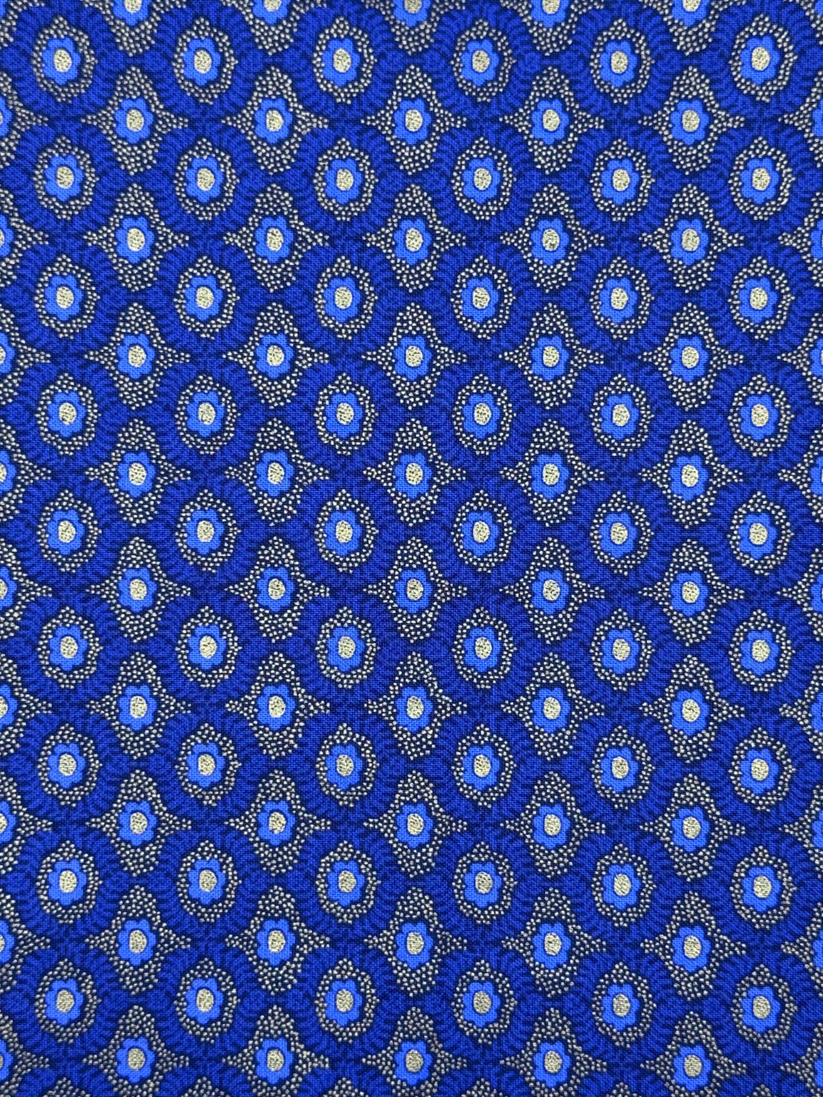 A close-up of a repeating blue patterned fabric or material with small circular motifs and fine dotted details in white, light blue, and gray.