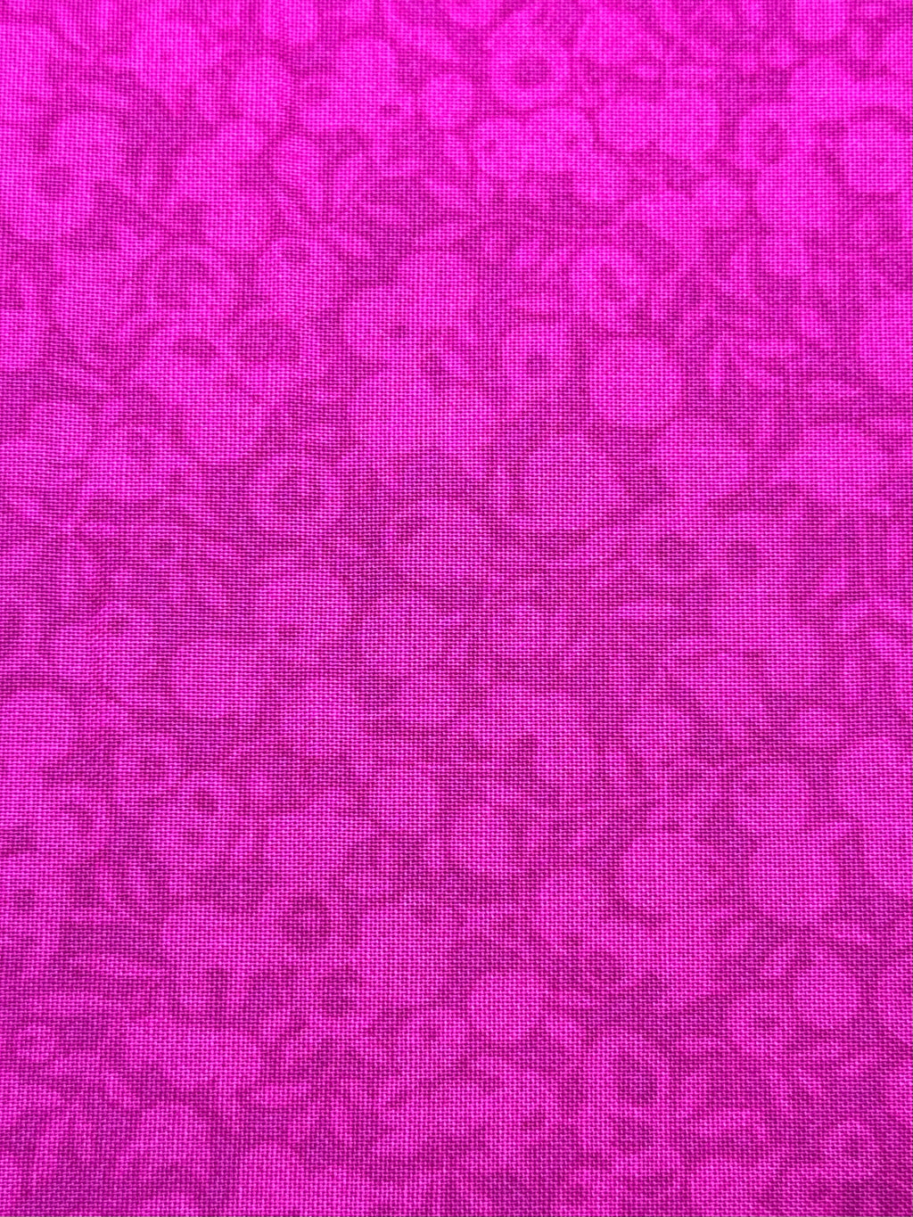 A close-up of a bright magenta pink fabric with a tonal floral pattern.