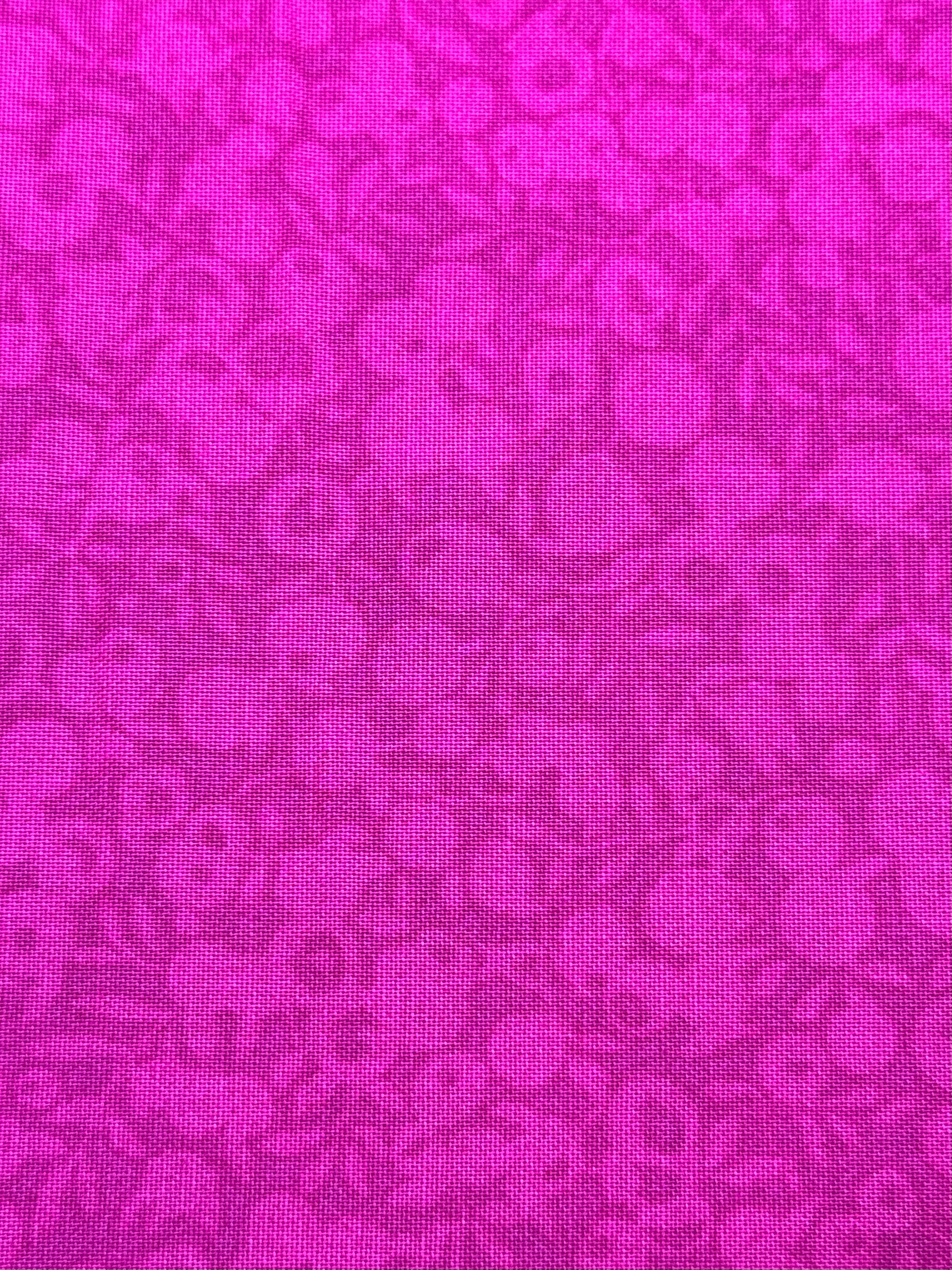 A close-up of a bright magenta pink fabric with a tonal floral pattern.
