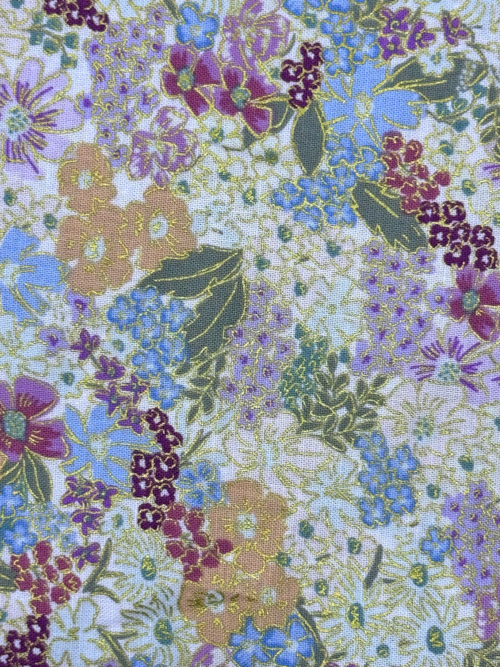 A close-up of a floral patterned fabric featuring purple, blue, and peach flowers with green leaves on a light background.