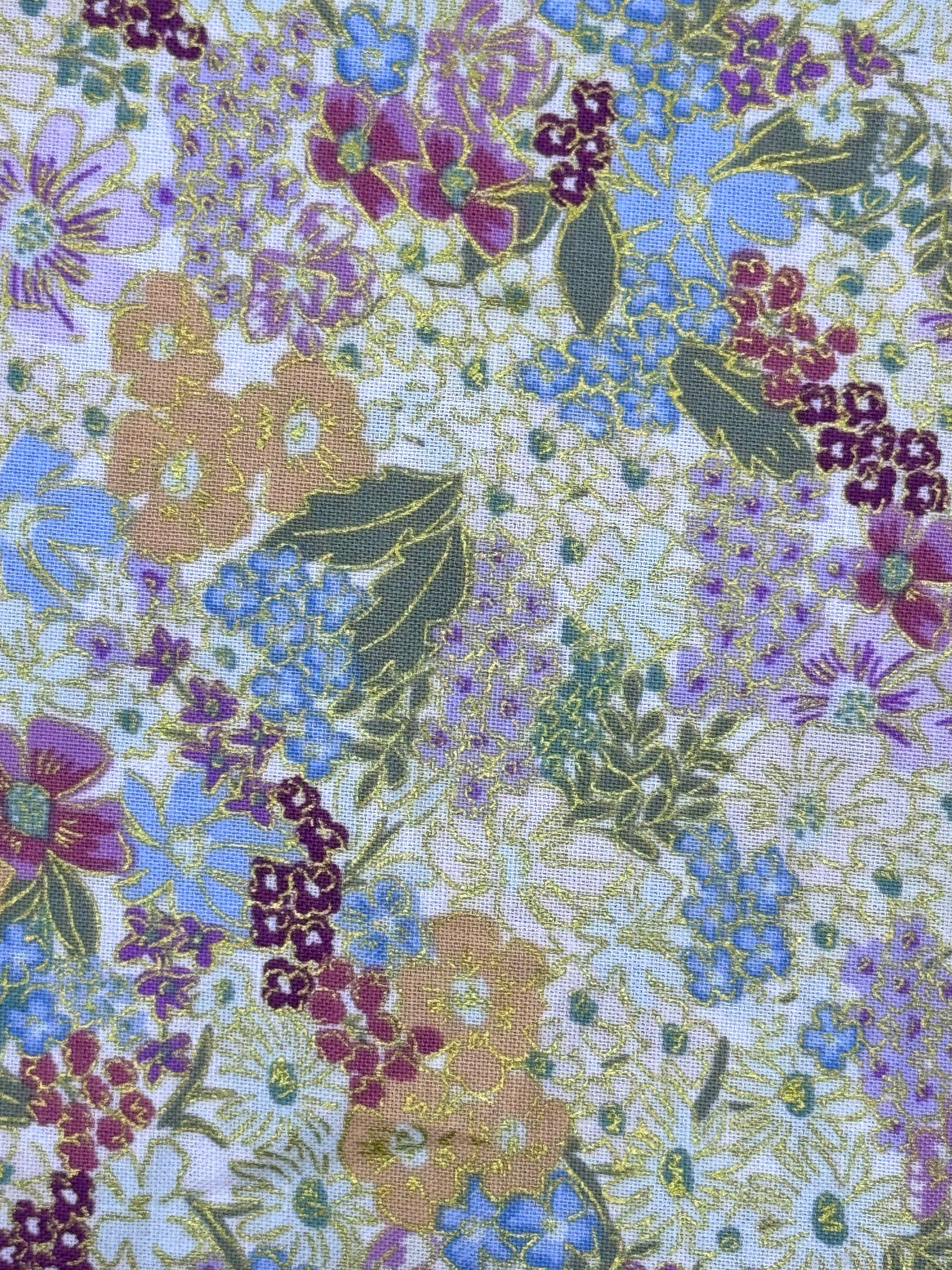 A close-up of a floral patterned fabric featuring purple, blue, and peach flowers with green leaves on a light background.