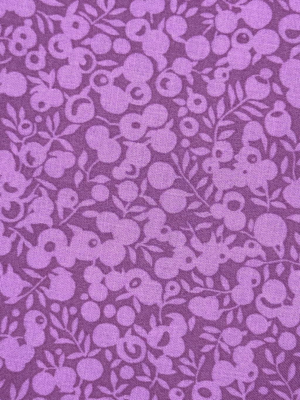 A close-up of a purple fabric with a repeating floral pattern in a slightly lighter lavender shade.