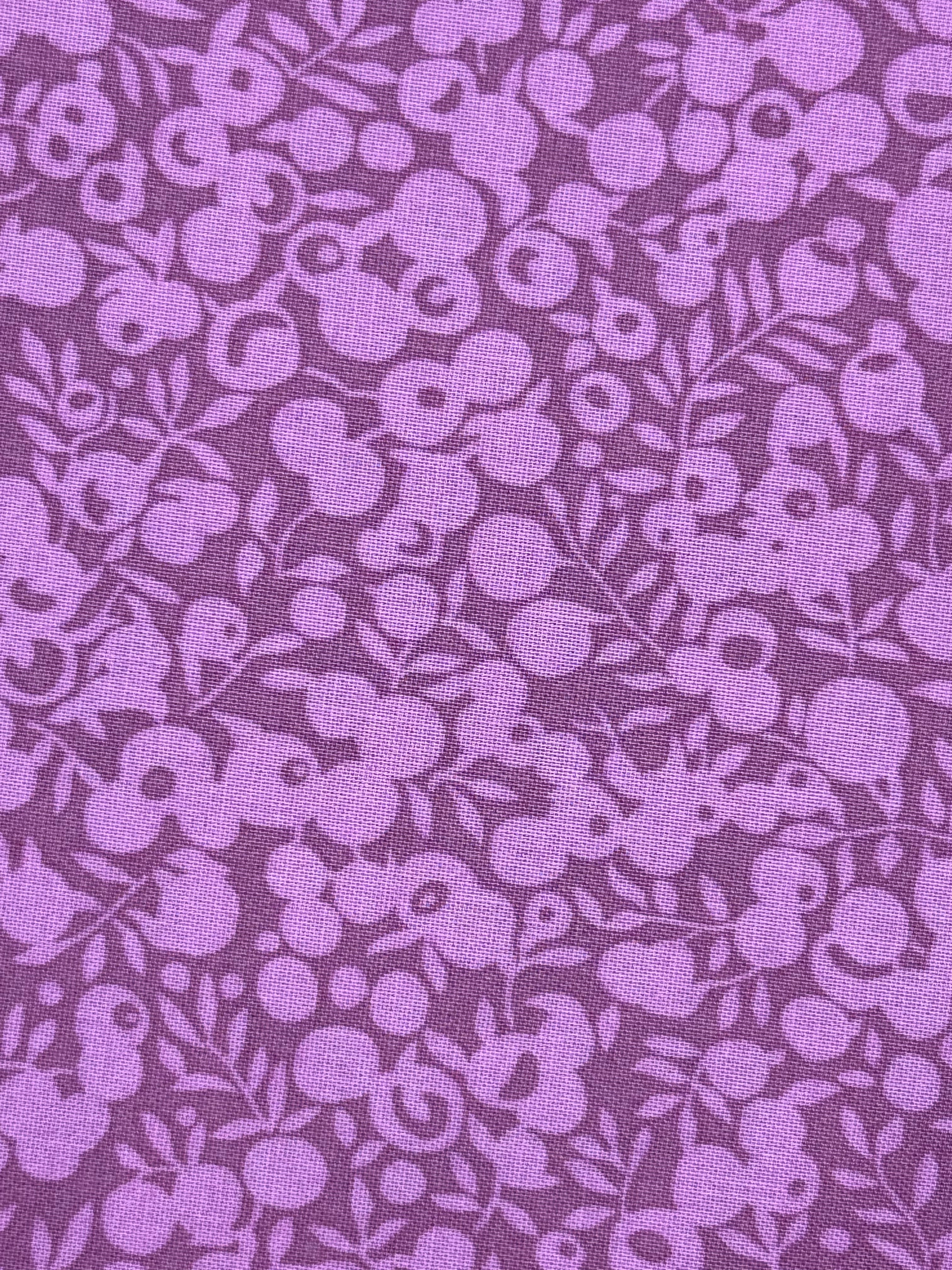 A close-up of a purple fabric with a repeating floral pattern in a slightly lighter lavender shade.