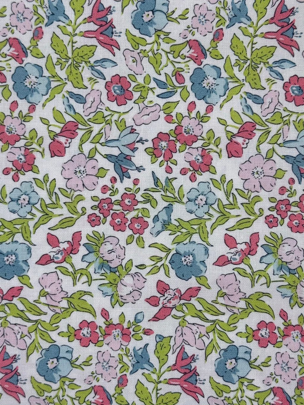 A close-up of a white fabric with a dense, colorful floral print featuring pink, blue, and red flowers with green leaves.