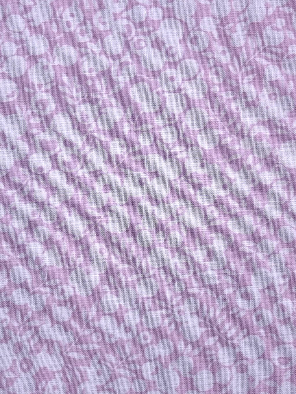 A close-up of pink fabric with a repeating white floral and berry pattern.