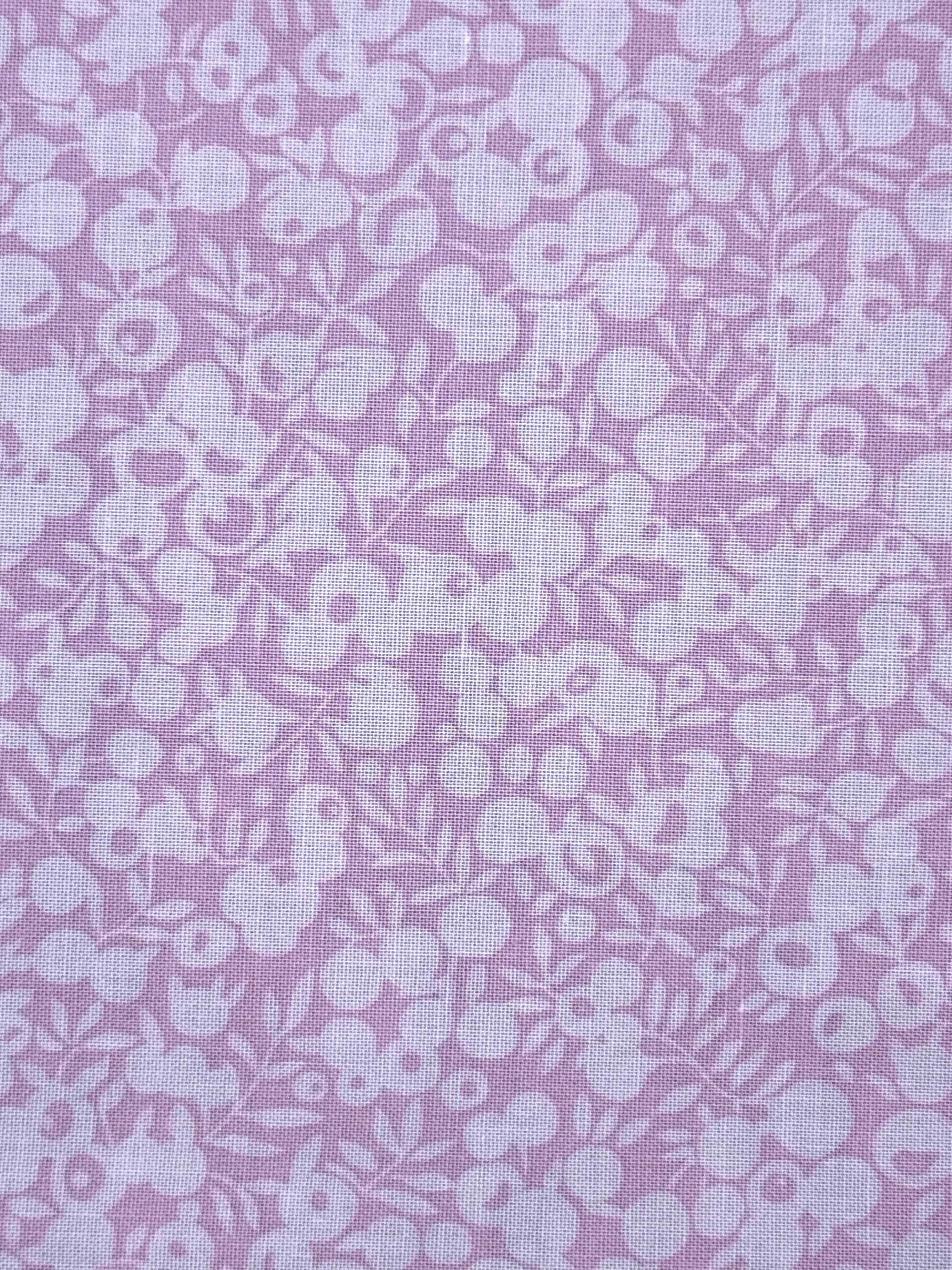 A close-up of pink fabric with a repeating white floral and berry pattern.