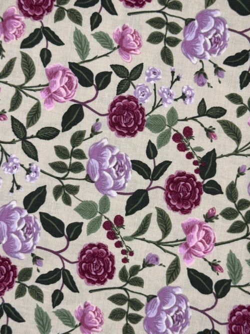 A close-up of a floral fabric pattern featuring large pink and purple roses, dark green leaves, and small berry clusters on a light beige background.