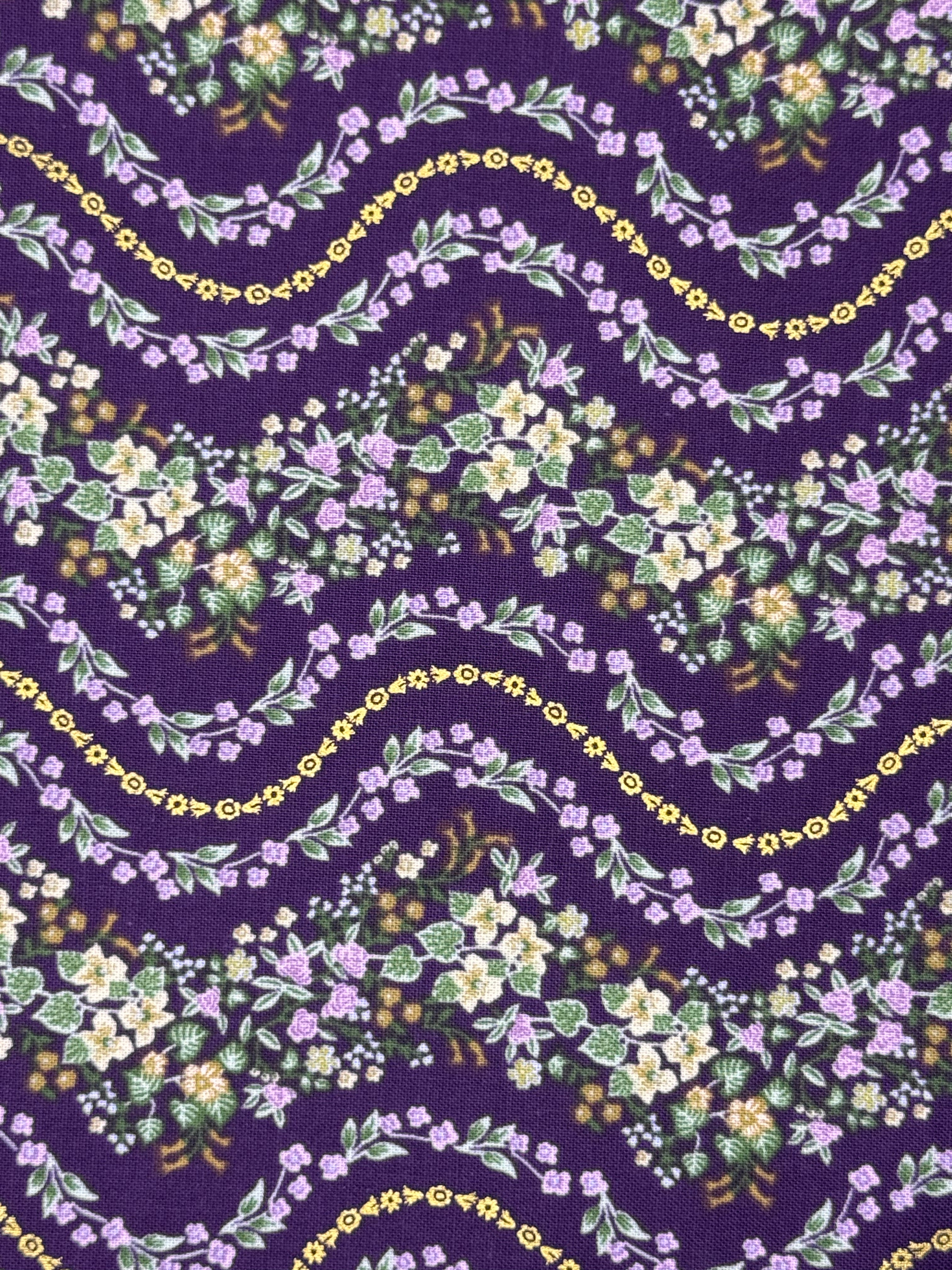 A close-up of a repeating floral pattern on fabric or wallpaper, featuring wavy garlands of small purple, white, and yellow flowers with green leaves on a deep purple background.