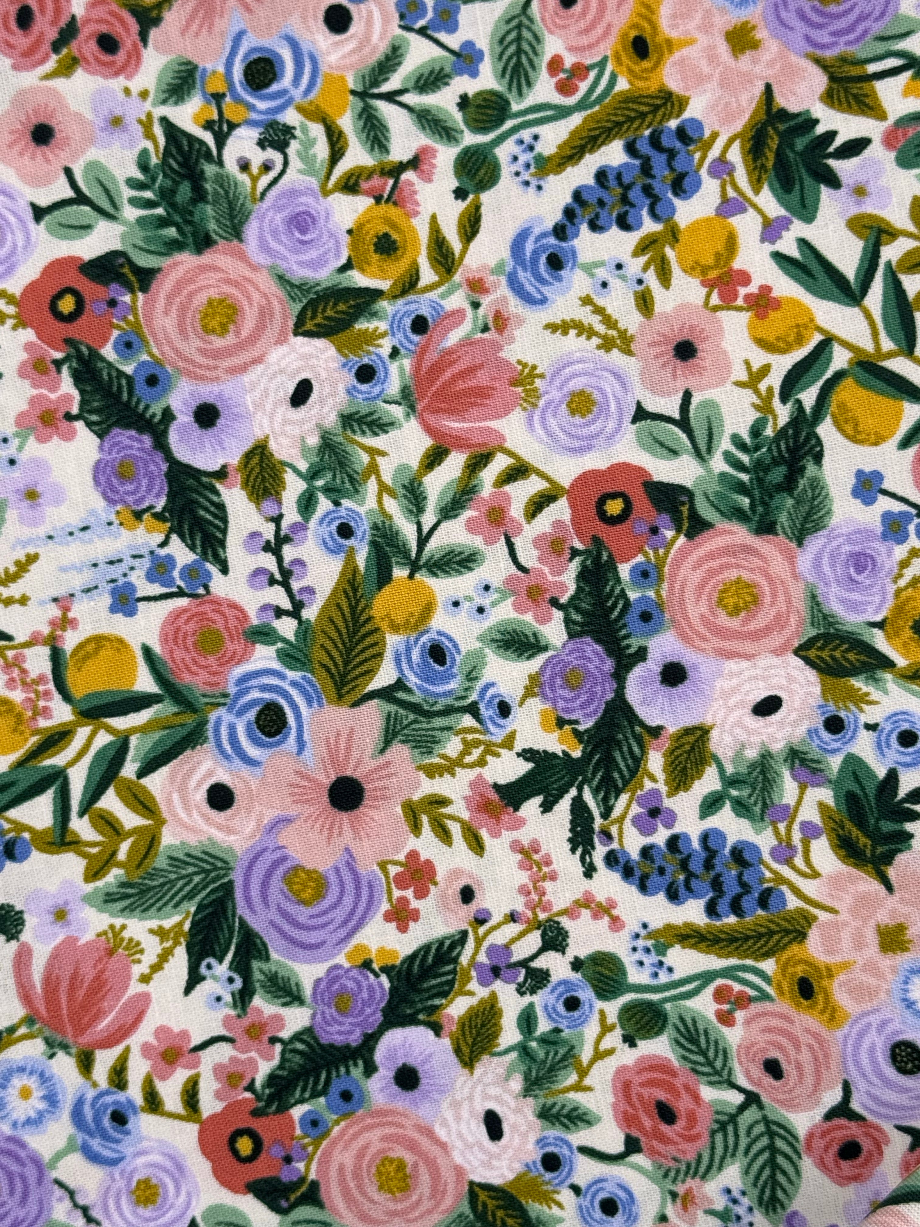 A close-up of a floral fabric pattern featuring pink, purple, blue, yellow, and green flowers and leaves on a white background.