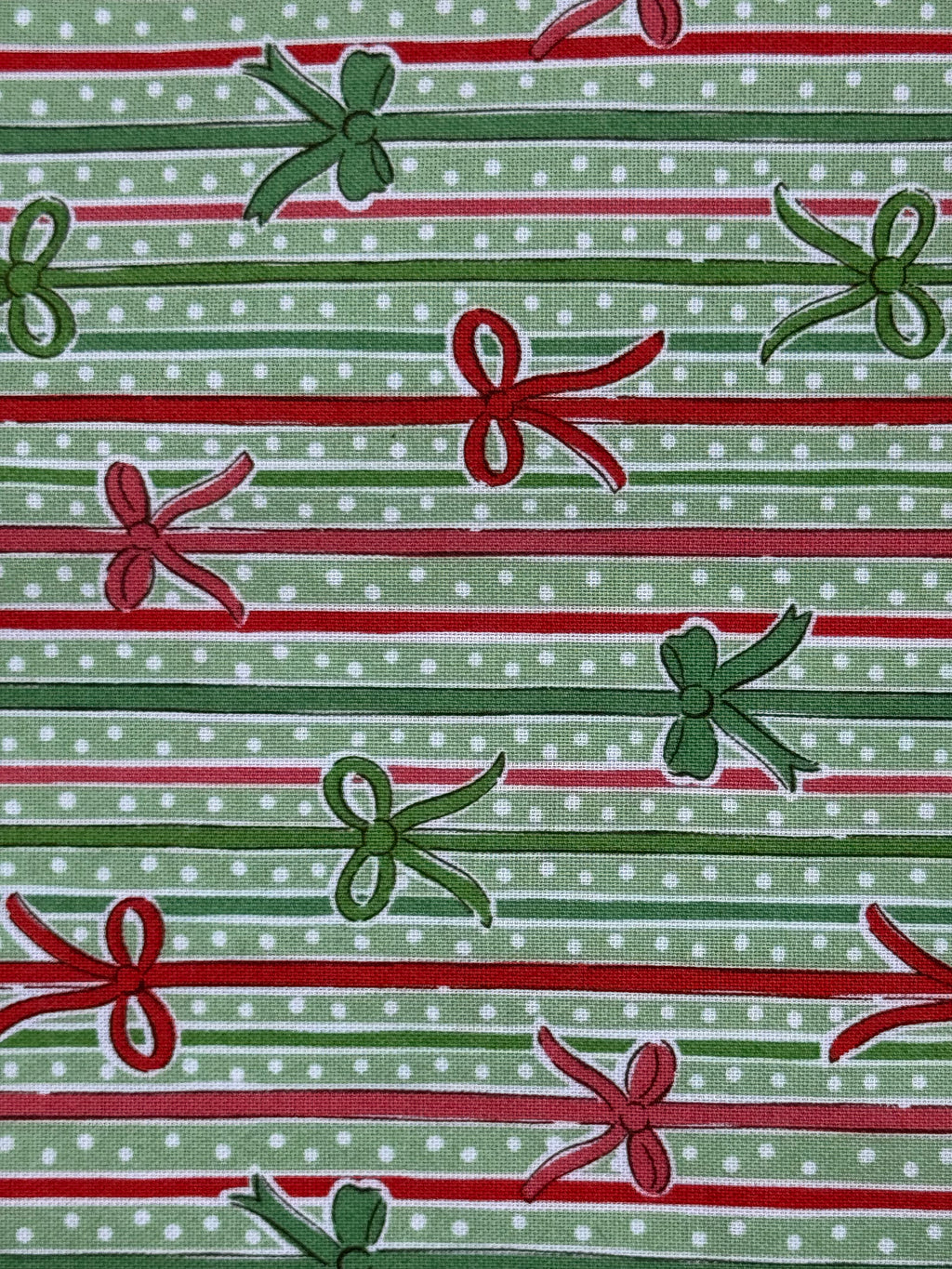 A close-up of a repeating holiday pattern featuring green and red gift bows and horizontal stripes on a light green polka-dot background.