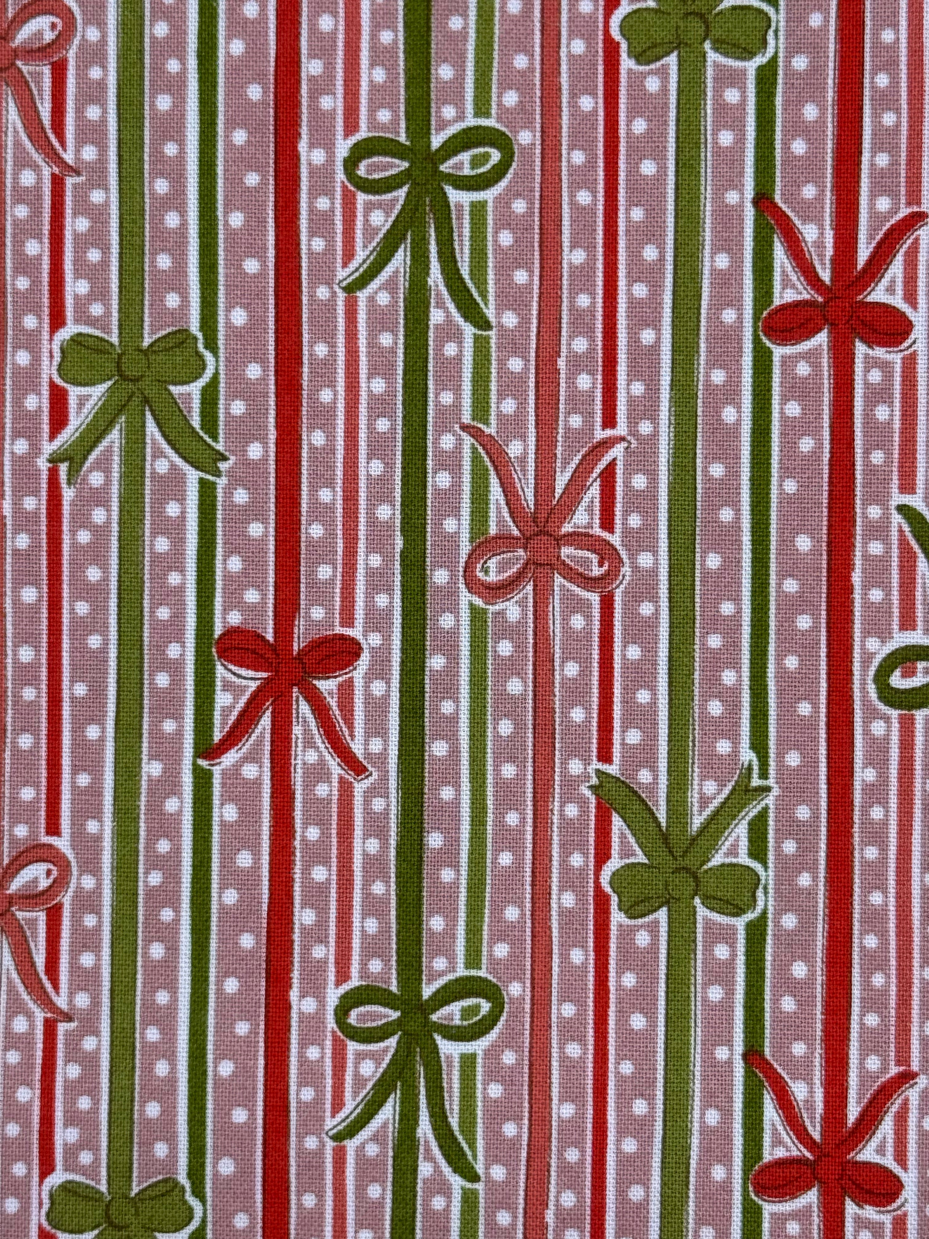 A close-up of a patterned fabric featuring vertical red and green stripes with white polka dots, interspersed with green and red ribbon-bow motifs.
