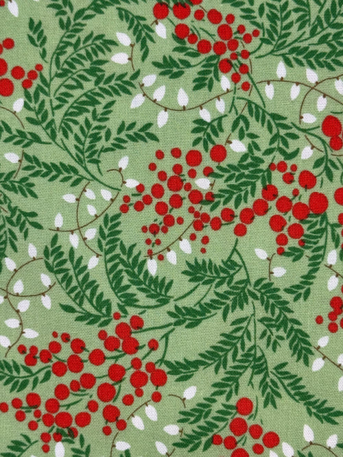 A close-up of a fabric pattern featuring green leaves and branches with clusters of red berries and small white leaf accents on a light sage green background.