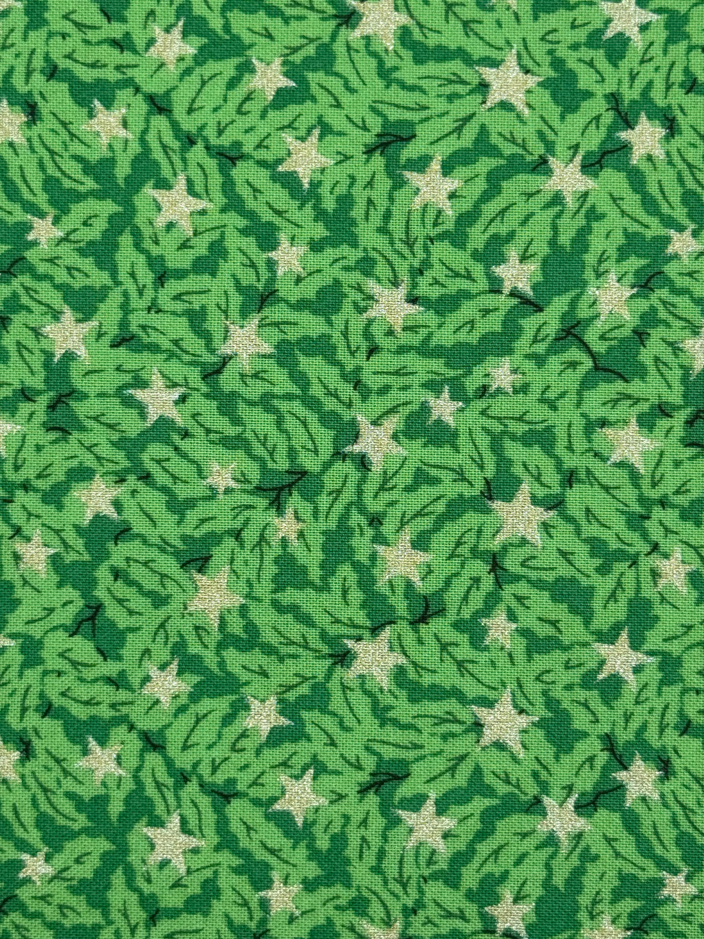 A close-up of a green patterned fabric featuring a repeating design of light green pine branches and cream-colored five-pointed stars.
