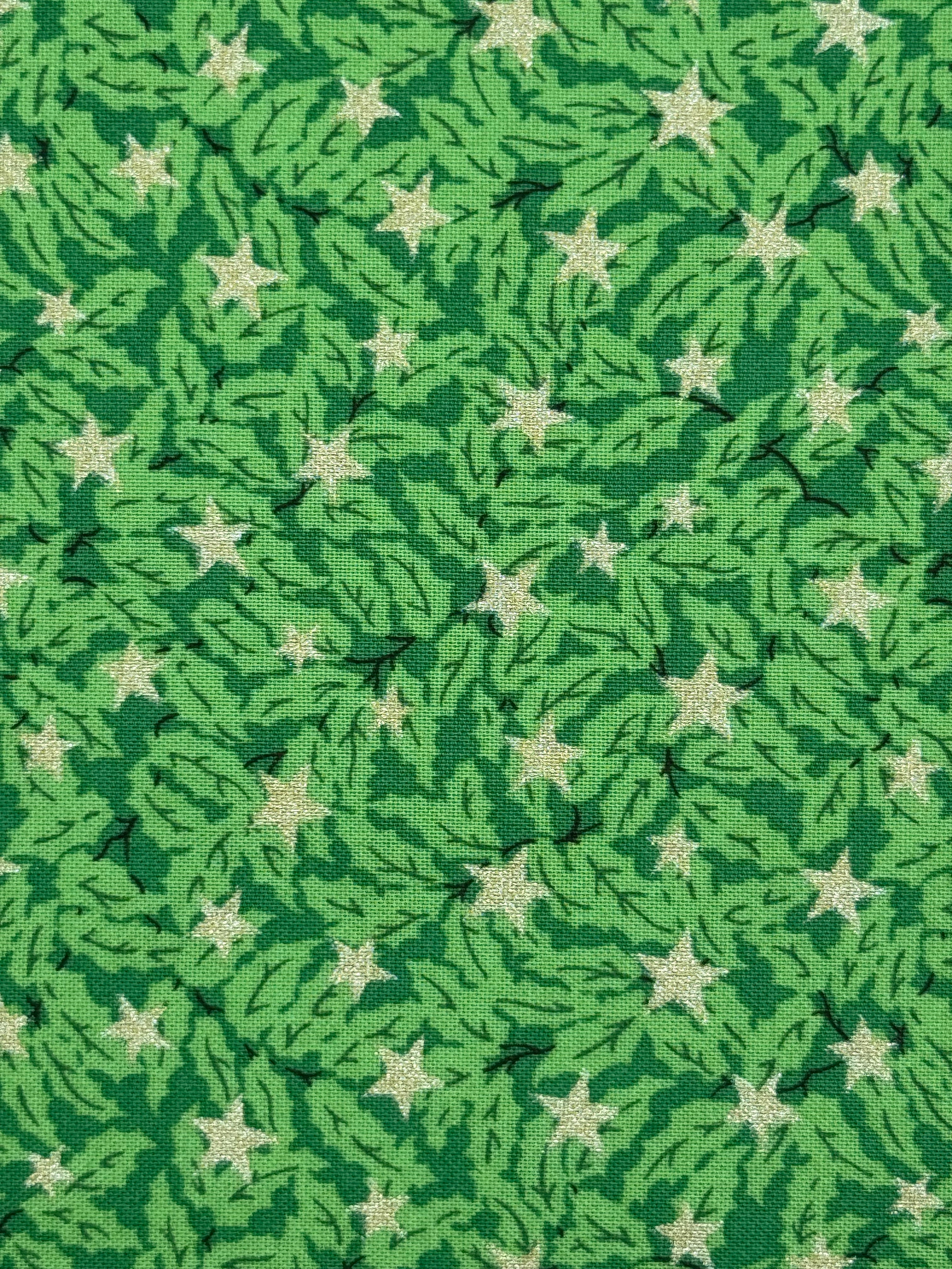 A close-up of a green patterned fabric featuring a repeating design of light green pine branches and cream-colored five-pointed stars.