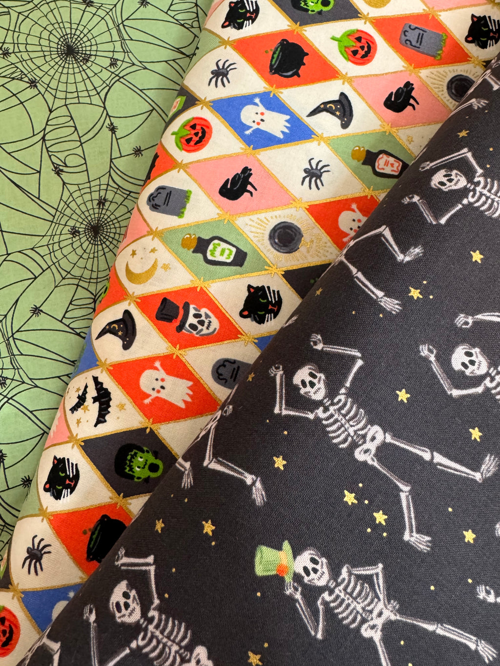Halloween-themed fabric with skeletons, ghosts, and pumpkins on a black background.