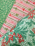 Three folded fabrics with holiday patterns displayed diagonally. The top-left fabric is green with small white stars and pine branches.