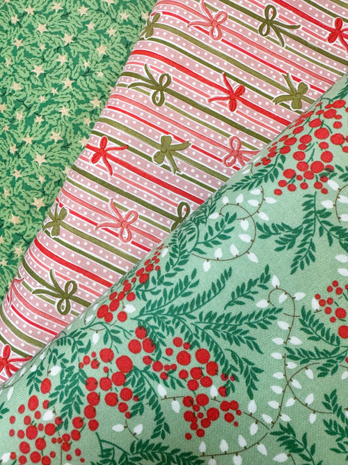 Three folded fabrics with holiday patterns displayed diagonally. The top-left fabric is green with small white stars and pine branches.