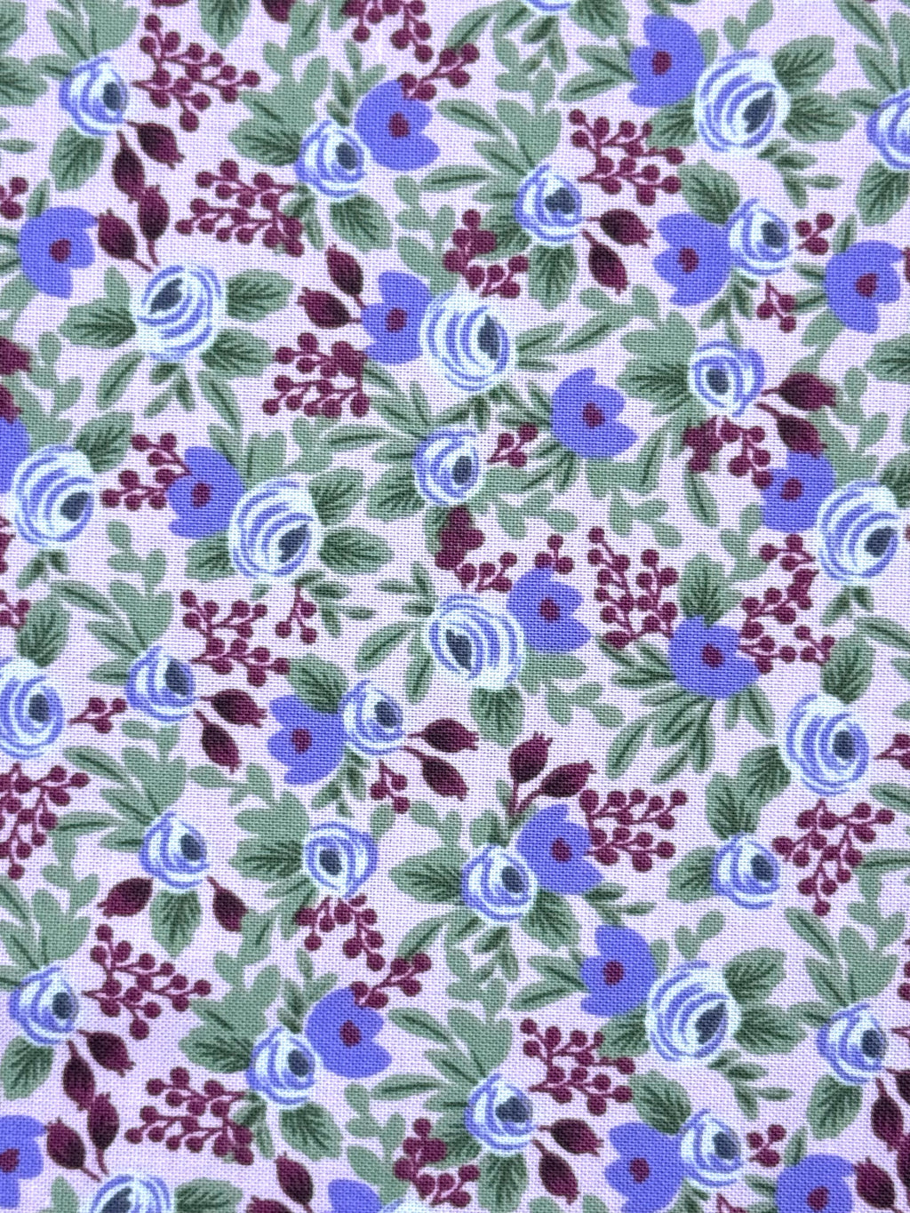 A close-up of a floral fabric pattern featuring blue and purple flowers with green leaves on a pale lavender background.