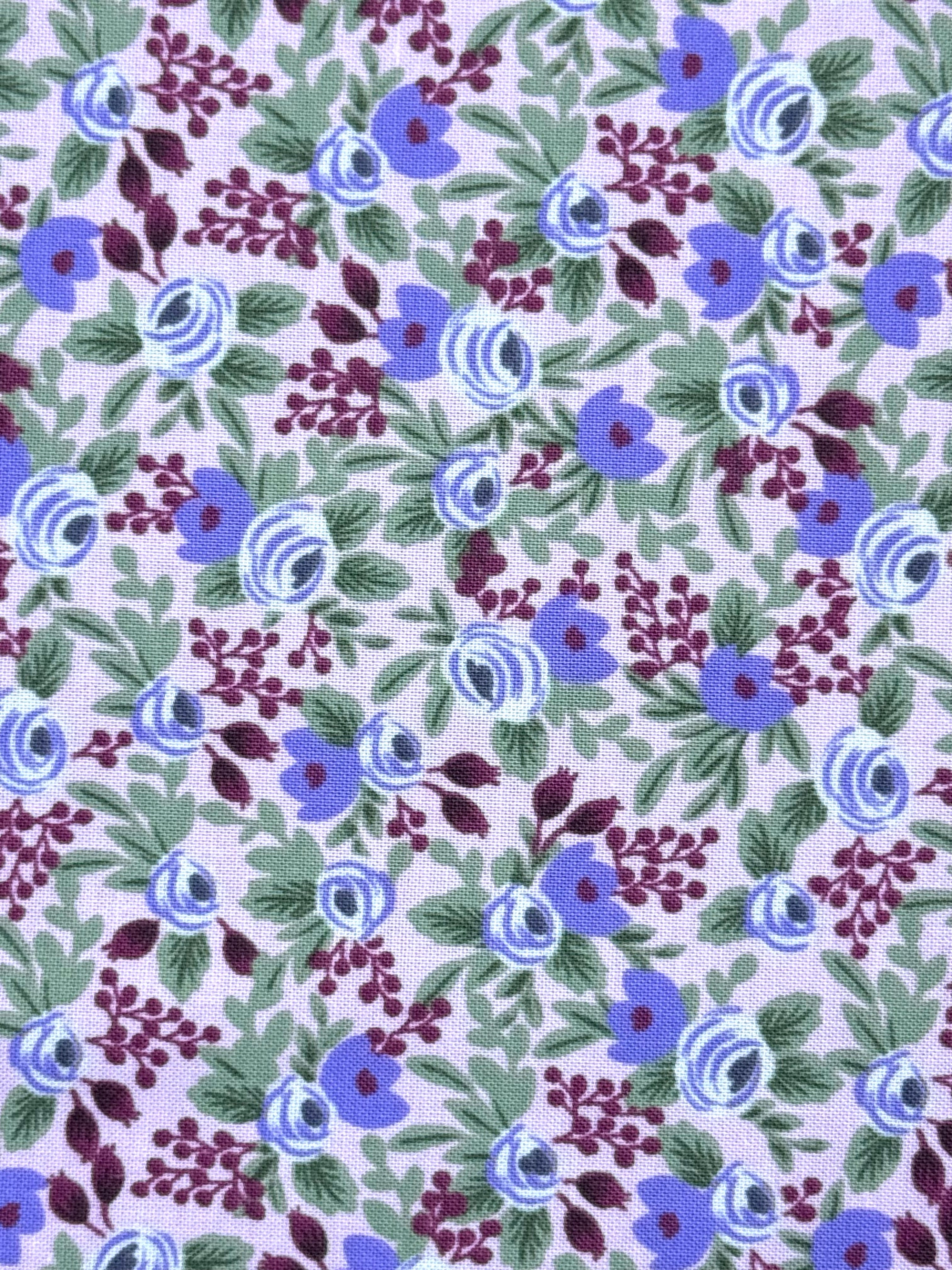 A close-up of a floral fabric pattern featuring blue and purple flowers with green leaves on a pale lavender background.